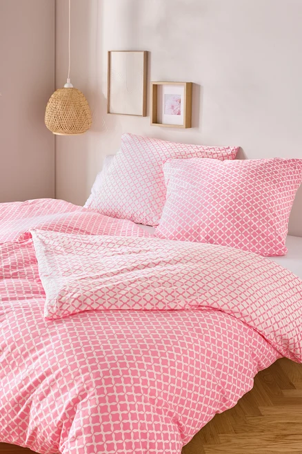 Gros plan d'un lit avec du linge de lit en jersey rose et blanc, taille standard et king size, avec deux oreillers et une couette.