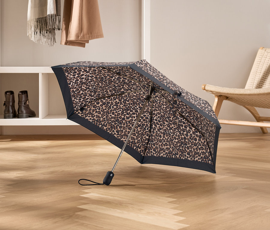 Parapluie ouvert à motif léopard posé sur un plancher en bois.