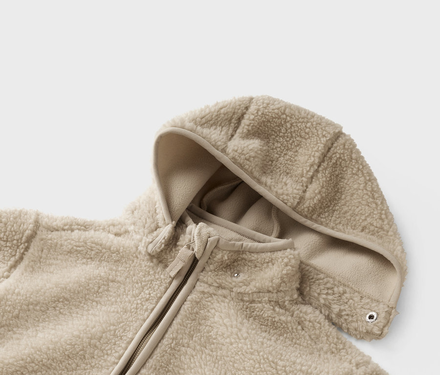 Gros plan d'une veste polaire teddy beige avec capuche et fermeture éclair.