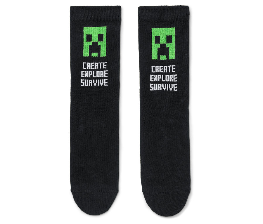 Deux chaussettes noires avec un visage de Creeper Minecraft vert et le texte « Create Explore Survive ».
