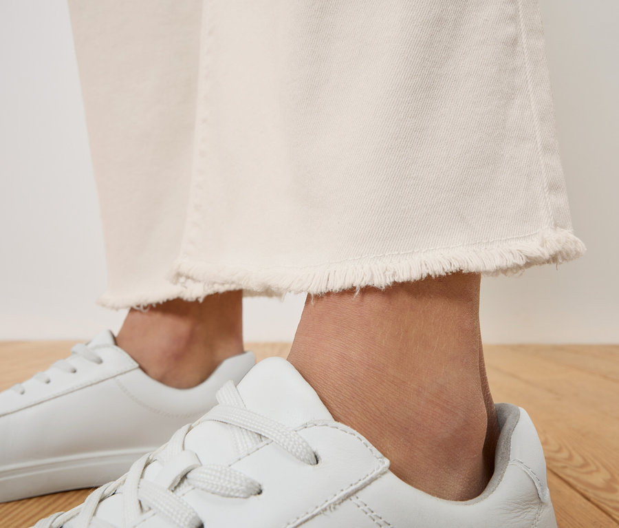 Gros plan d'une personne portant un jean blanc à franges et des baskets blanches.