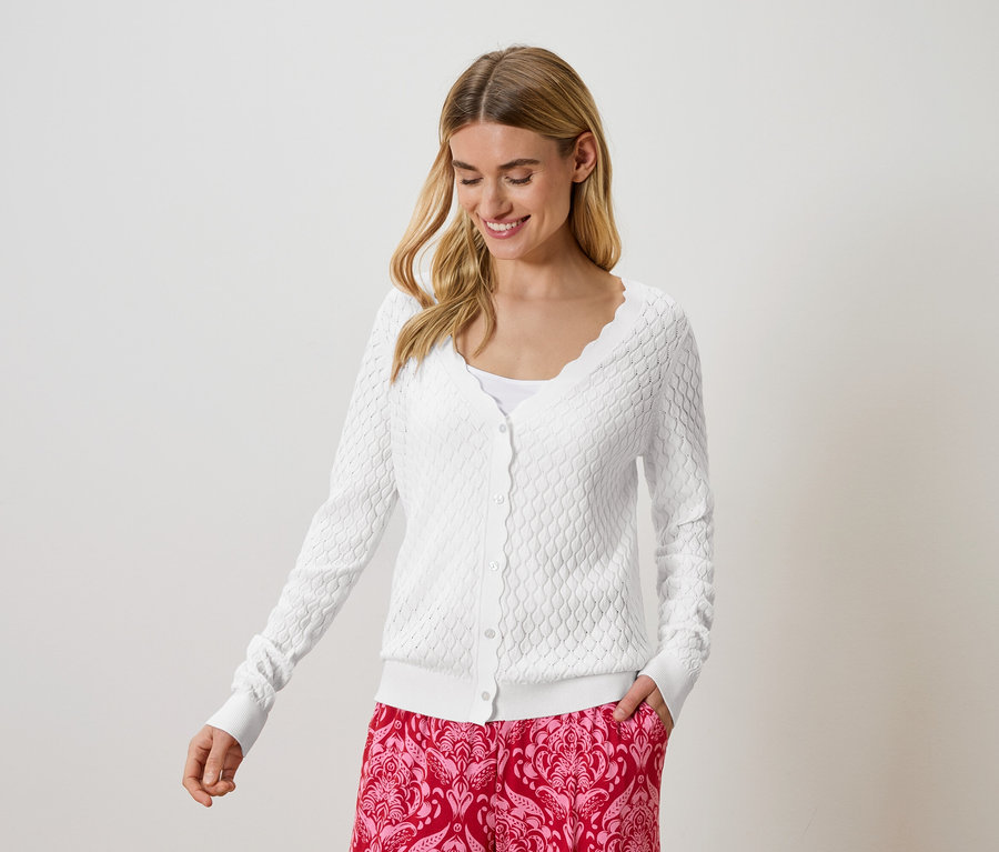 Femme portant un cardigan tricoté blanc et un pantalon à motifs rouges.