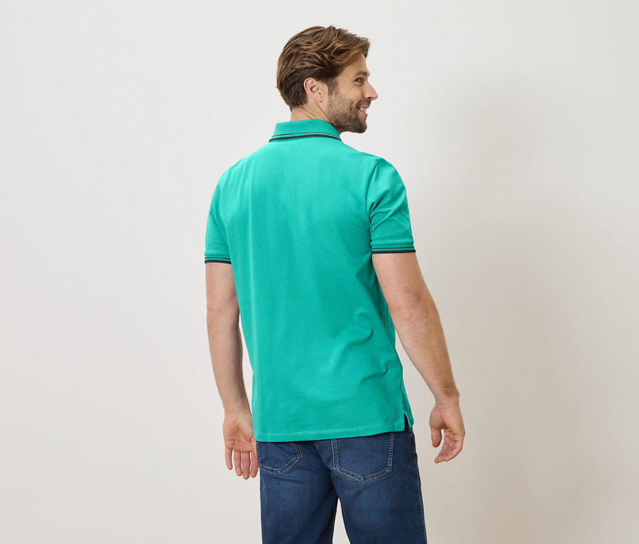 Un homme vu de dos portant un polo vert et un jean.