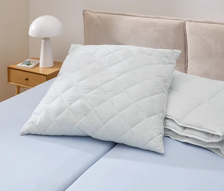Un oreiller Cell Solution® blanc matelassé (90 x 70 cm) est posé sur un lit bleu clair. À côté se trouvent d'autres oreillers Cell Solution® (80 x 80 cm, 100 x 65 cm).