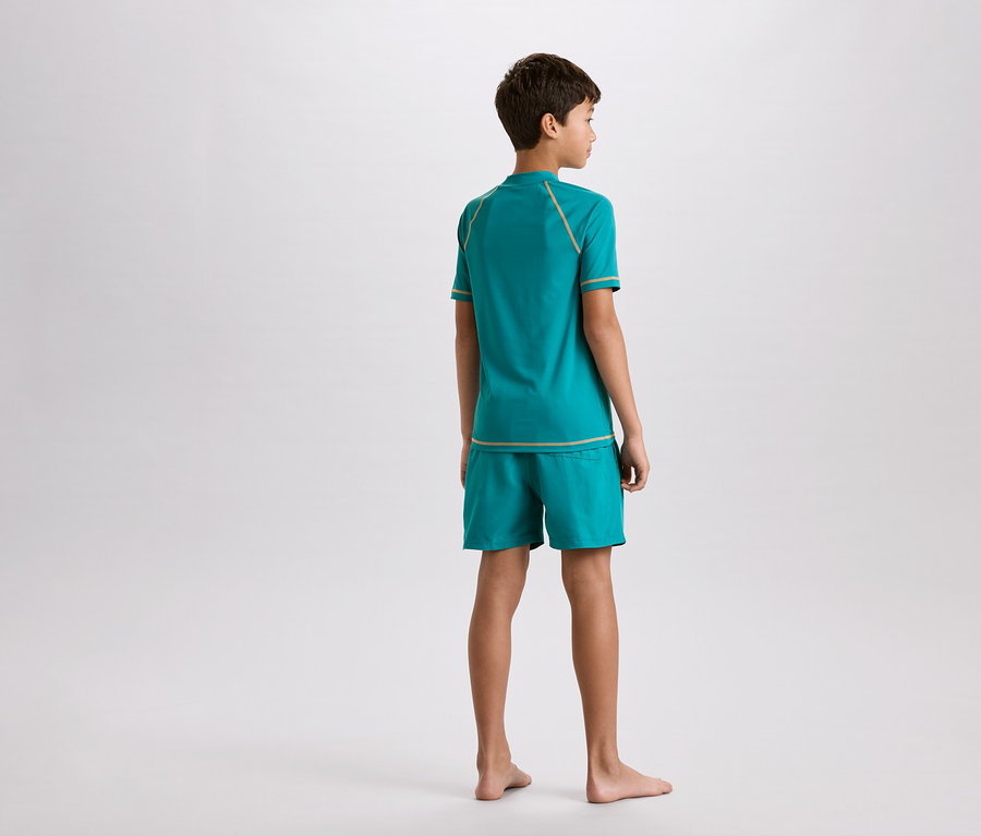 Garçon vu de dos, portant un t-shirt turquoise et un short avec des coutures décoratives dorées.