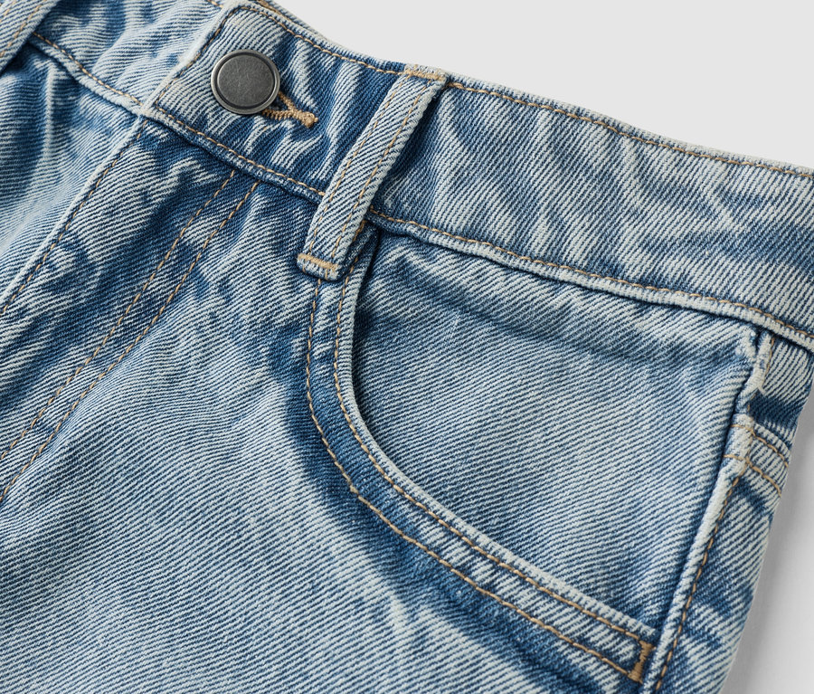 Gros plan d'un jean bleu clair avec bouton et poche.