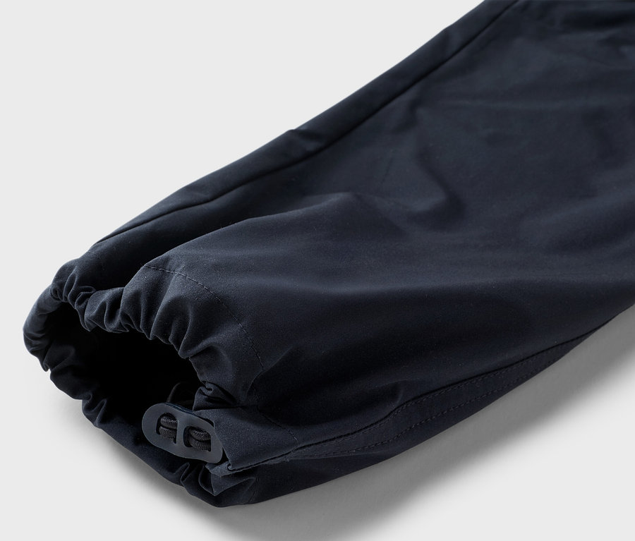 Gros plan sur une jambe de pantalon bleu marine avec un ourlet élastique et une fermeture à bascule réglable sur un fond neutre.