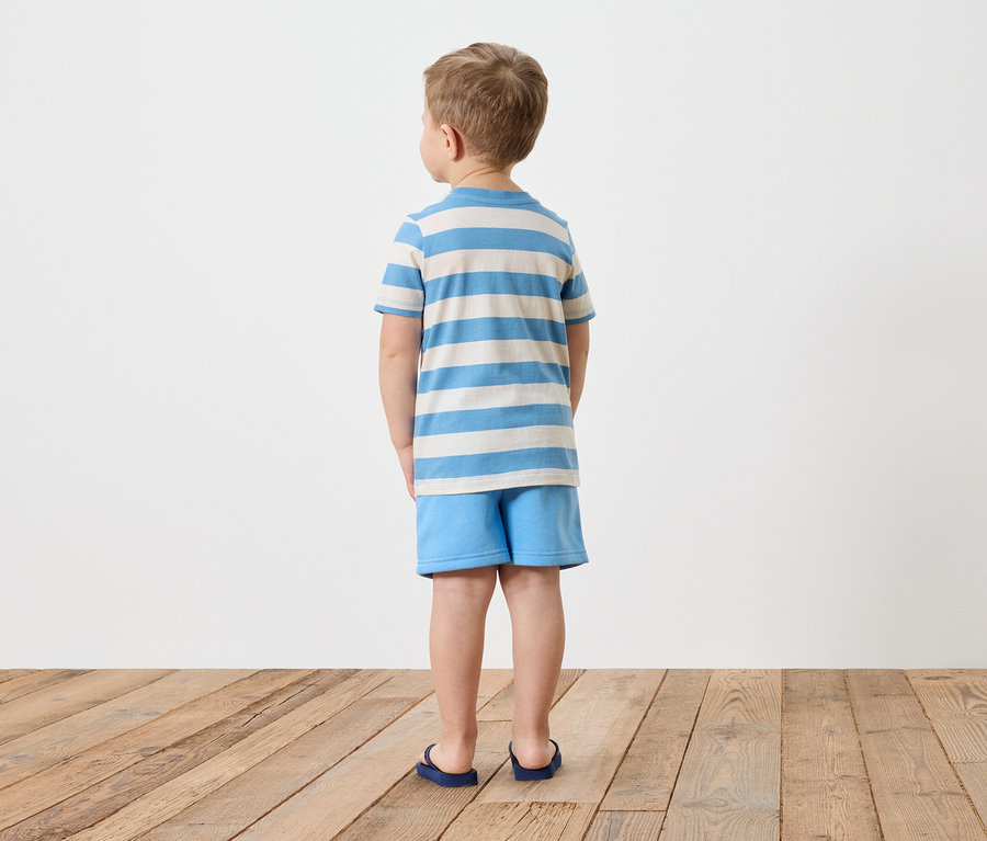 Un garçon se tient dos à la caméra, il porte un t-shirt rayé et un short bleu.