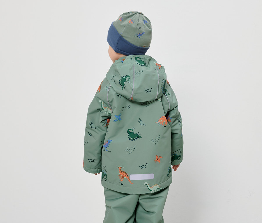 Vue arrière d'un enfant portant un bonnet et une combinaison verte à motif de dinosaures sur fond blanc.