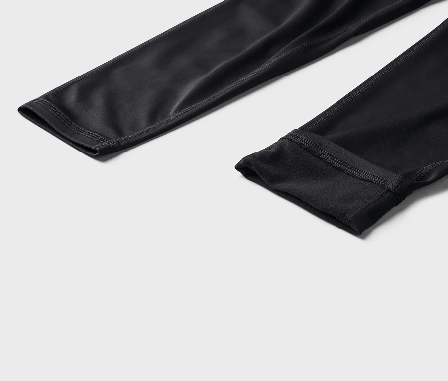 Gros plan de deux jambes de pantalon noires et moulantes avec des coutures visibles sur un fond gris.