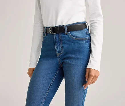 Une personne porte un jean bleu avec une ceinture noire et un haut blanc.