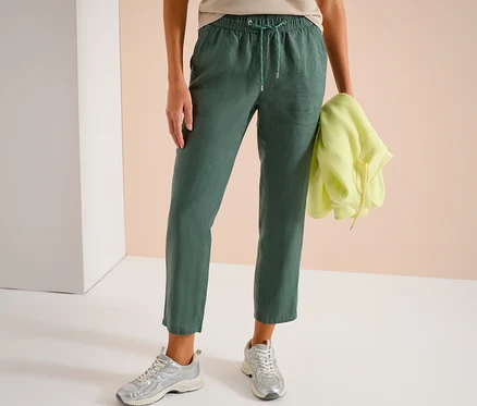 Femme portant un pantalon vert à cordon et des baskets argentées, tenant un sweat à capuche jaune.
