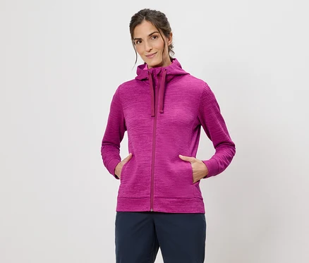Femme portant un sweat à capuche rose, les mains dans les poches, sur un fond blanc.