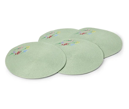 Quatre sets de table ronds vert clair avec des motifs floraux brodés sont posés les uns sur les autres.