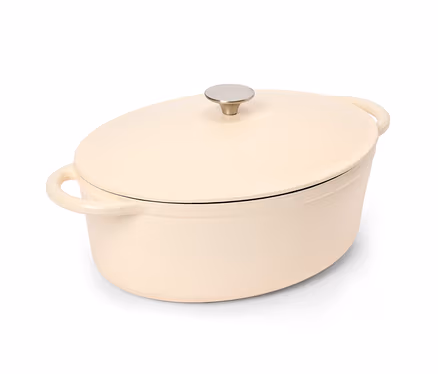 Une cocotte ovale de couleur crème avec un couvercle et deux poignées, dotée d'un bouton argenté sur le dessus, sur fond blanc.