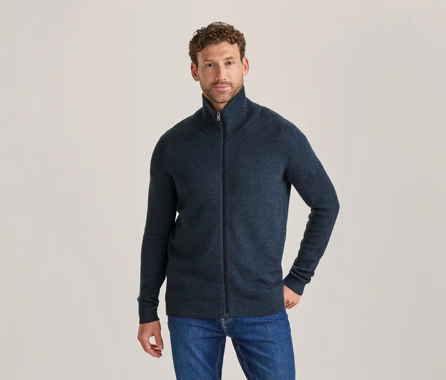 Homme portant un cardigan zippé bleu foncé et un jean bleu, debout et regardant l'appareil photo.