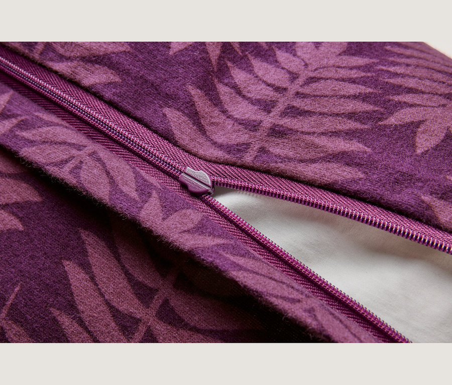 Gros plan d'un tissu violet avec un motif de feuilles plus foncé, montrant une fermeture éclair violette assortie partiellement ouverte, révélant un matériau blanc en dessous.