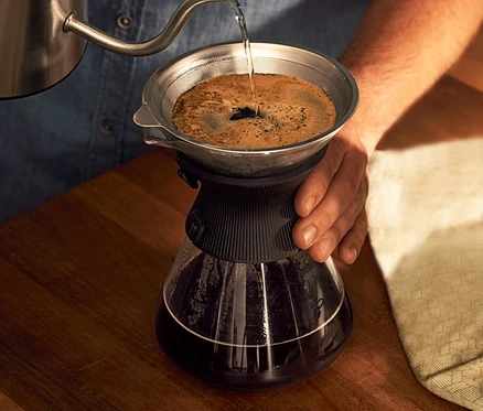 Un homme verse de l'eau dans une carafe en verre BEEM Pour Over, 0,75 l avec filtre à café.