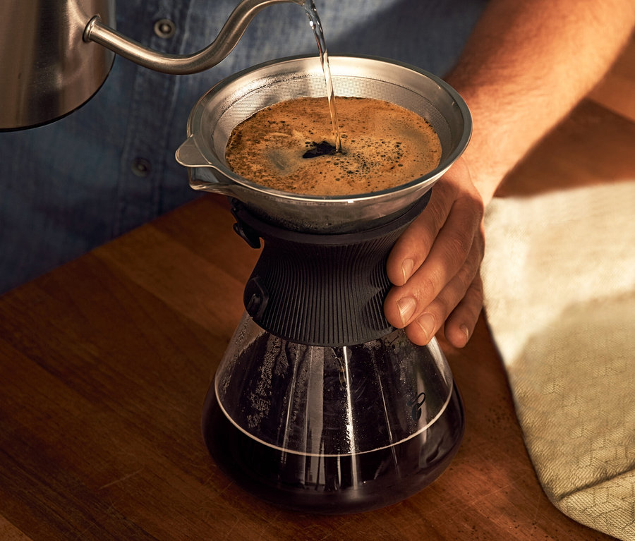 Un homme verse de l'eau dans une carafe en verre BEEM Pour Over, 0,75 l avec filtre à café.