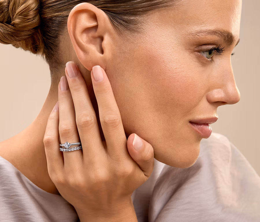 Une femme aux cheveux attachés touche son visage et montre une bague.