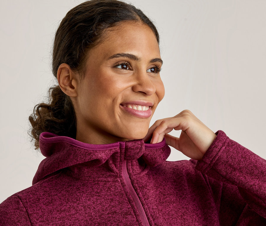 Une femme souriante aux cheveux foncés ajuste le col de sa veste à capuche magenta.
