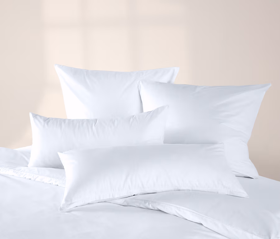 Quatre taies d'oreiller en jersey blanc cassé sur un lit avec de la literie blanche.