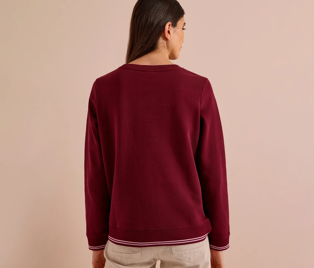 Femme de dos portant un sweatshirt CECIL bordeaux avec des rayures blanches aux poignets et à l'ourlet, et un pantalon clair.