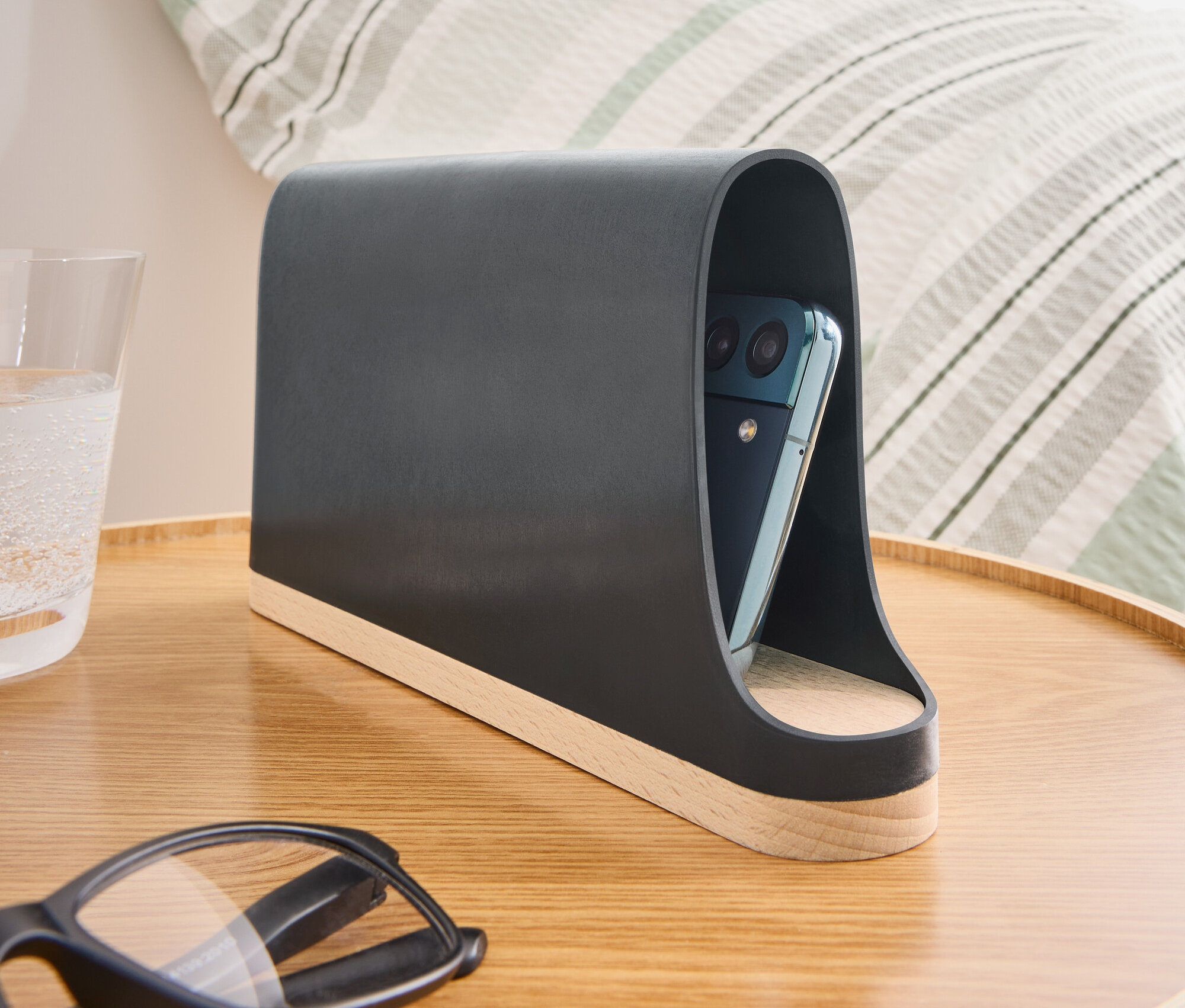 Sur une table de chevet, il y a un support de téléphone gris foncé avec une base en bois et un téléphone à l'intérieur.