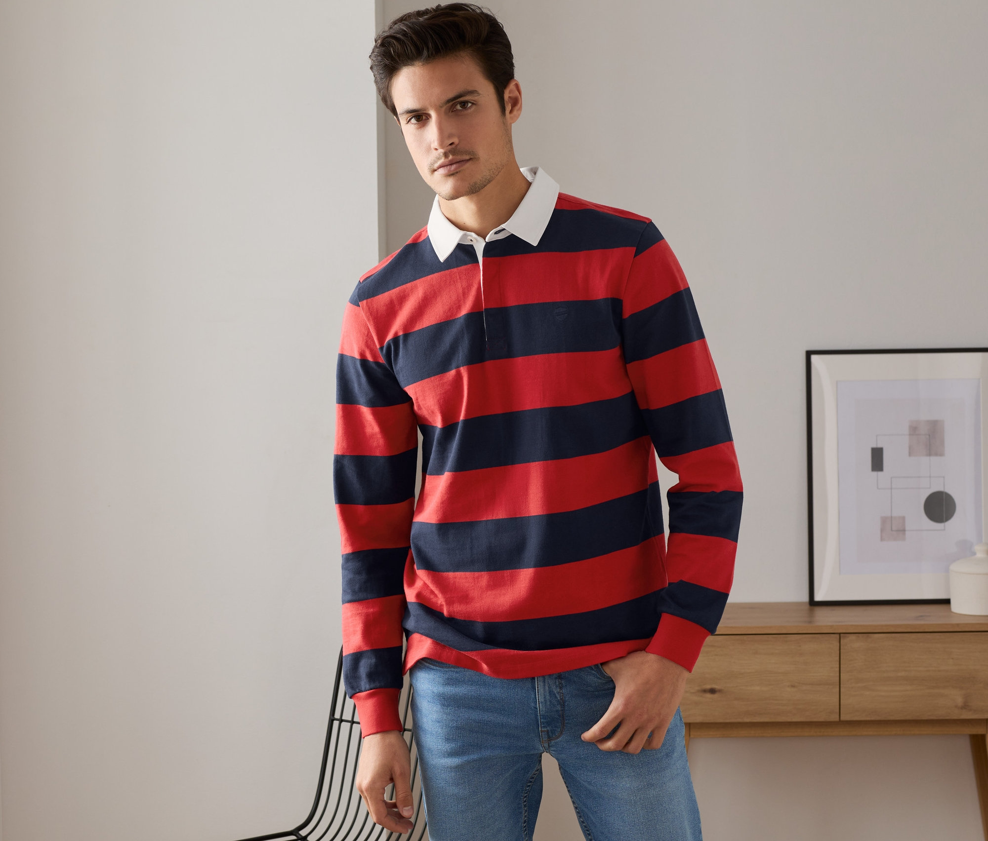 Homme posant en polo manches longues bleu marine et rouge.