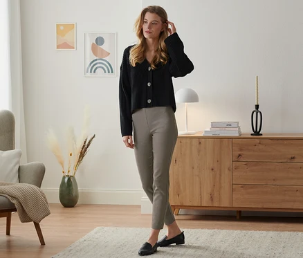 Une femme se tient dans un salon et porte une veste noire et un pantalon stretch.