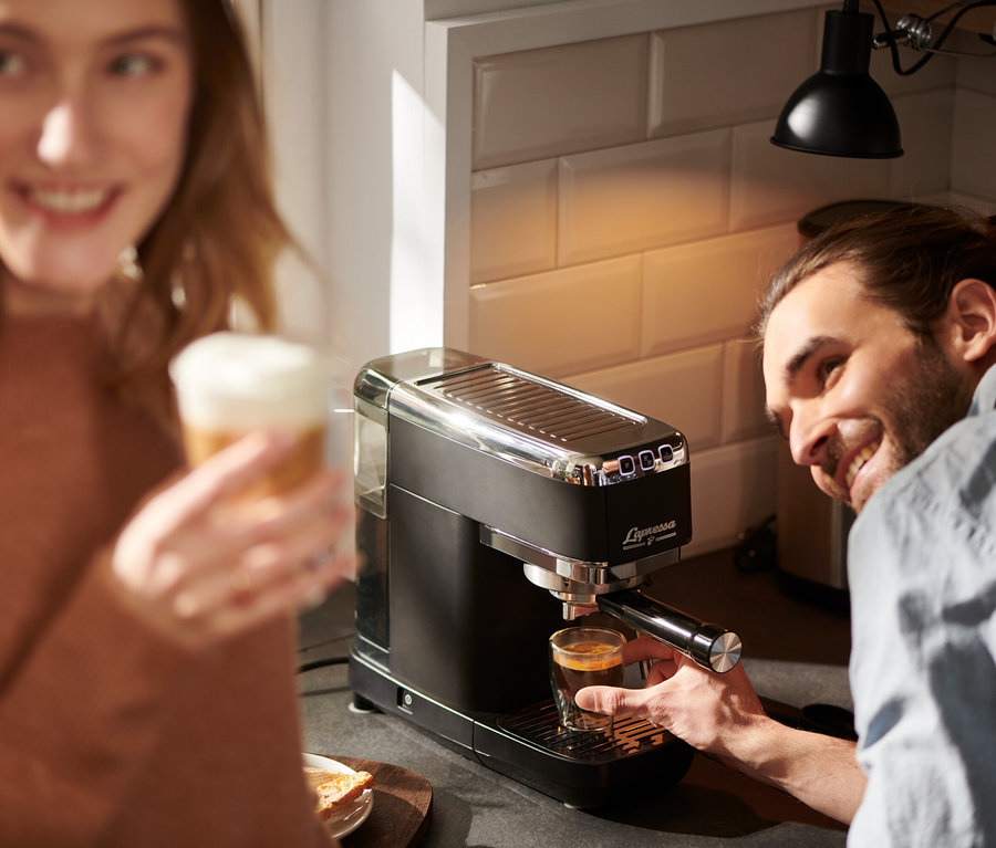 Un homme prépare un espresso avec une machine à porte-filtre « Lapressa » noire, une femme tient un latte.