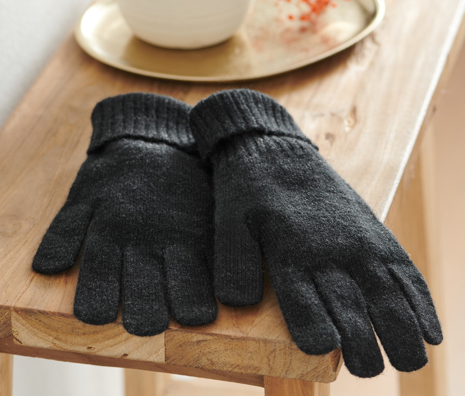 Une paire de gants en maille anthracite avec de la laine est posée sur un tabouret en bois.