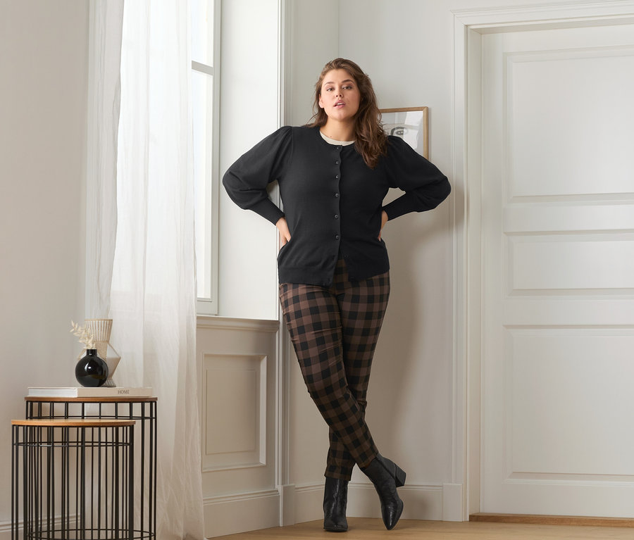 Femme posant en jaquette en maille fine avec manches bouffantes, pantalon stretch à carreaux et bottines en cuir.