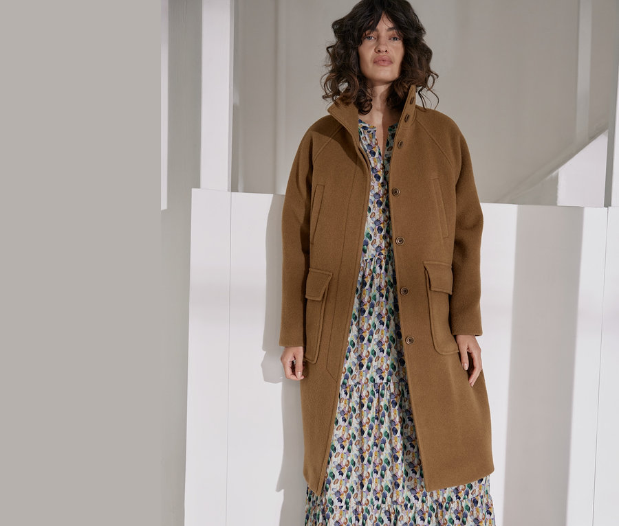 Femme posant en manteau NAH/STUDIO en laine recyclée camel et robe maxi.