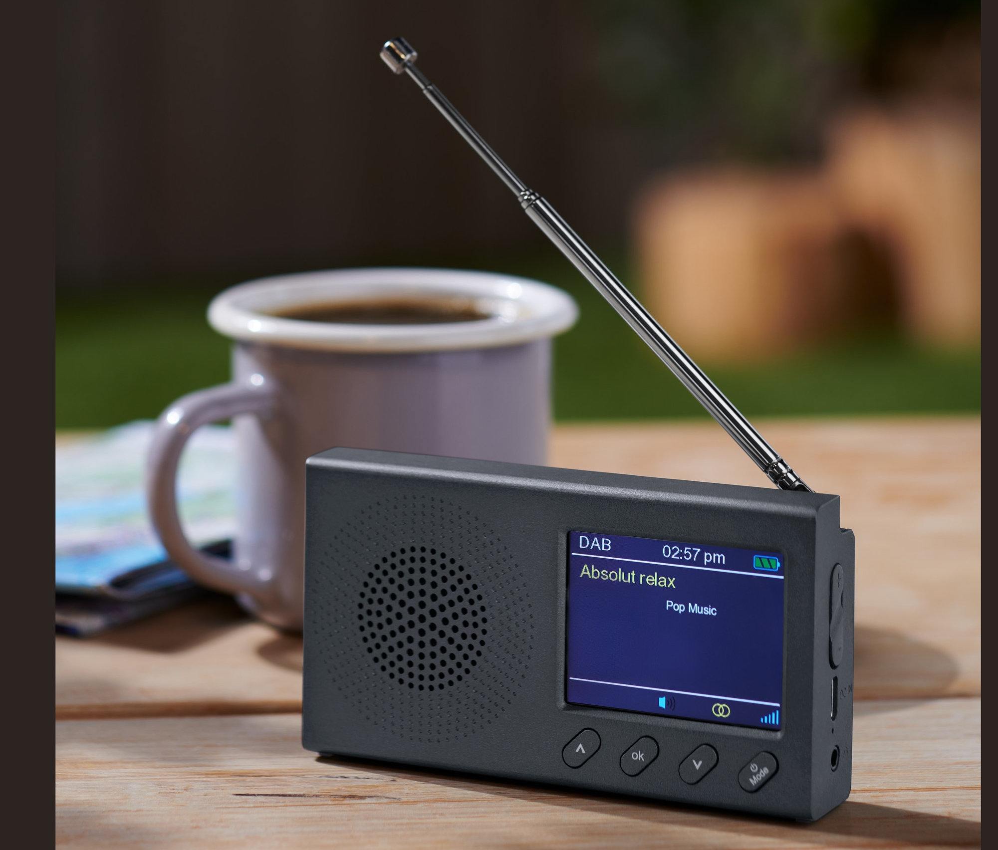 Une radio portable DAB/FM noire avec Bluetooth est posée sur une table en bois à côté d'une tasse de café.