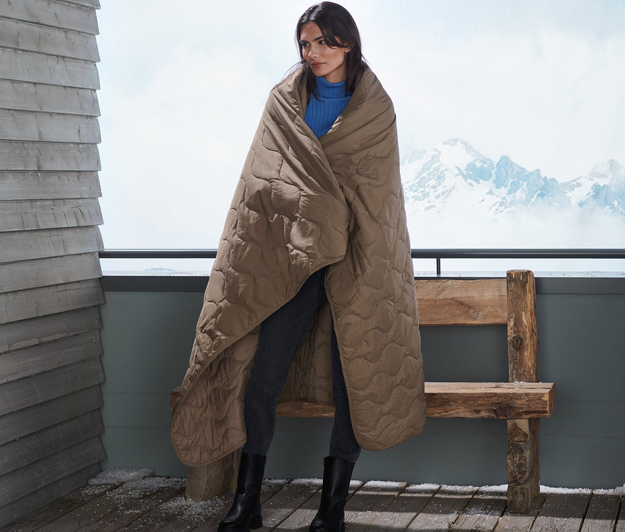 Femme debout sur un balcon enveloppée dans une couverture thermique.