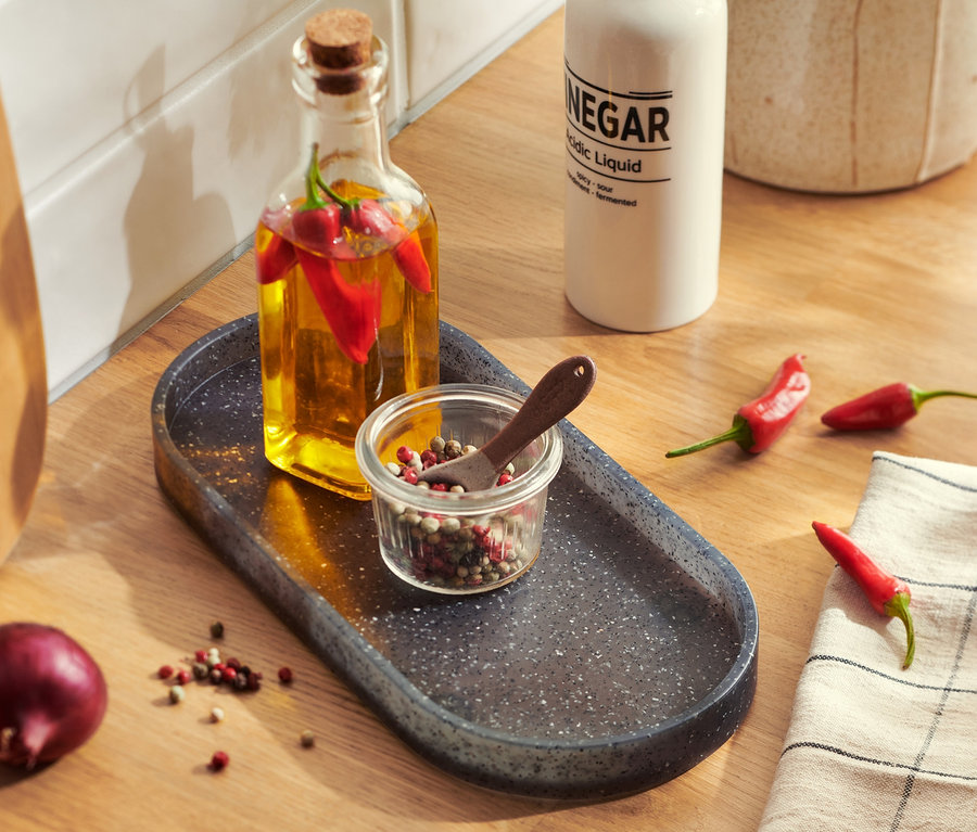 Sur un comptoir de cuisine, il y a un comptoir de cuisine aspect granit avec une bouteille d'huile, des piments et un pot à épices.