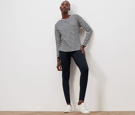 Femme posant sur un plancher en bois en legging noir et un haut rayé.