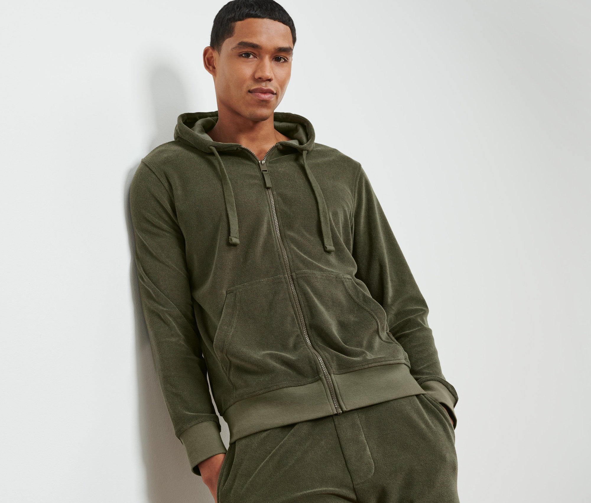 Un homme appuyé contre un mur porte un sweat-shirt à capuche en tissu éponge.