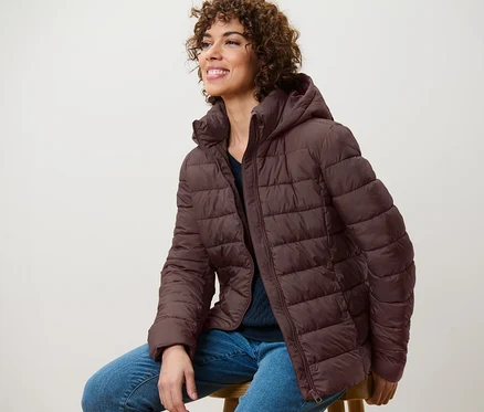 Femme assise sur un tabouret portant une veste matelassée à capuche marron foncé.