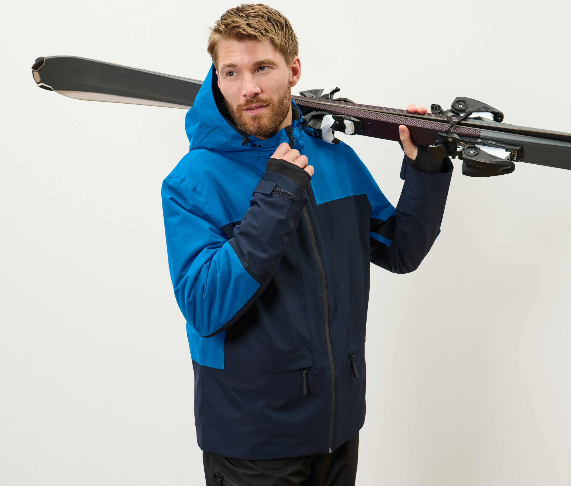 Un homme portant une veste de ski bleue tient des skis sur son épaule.