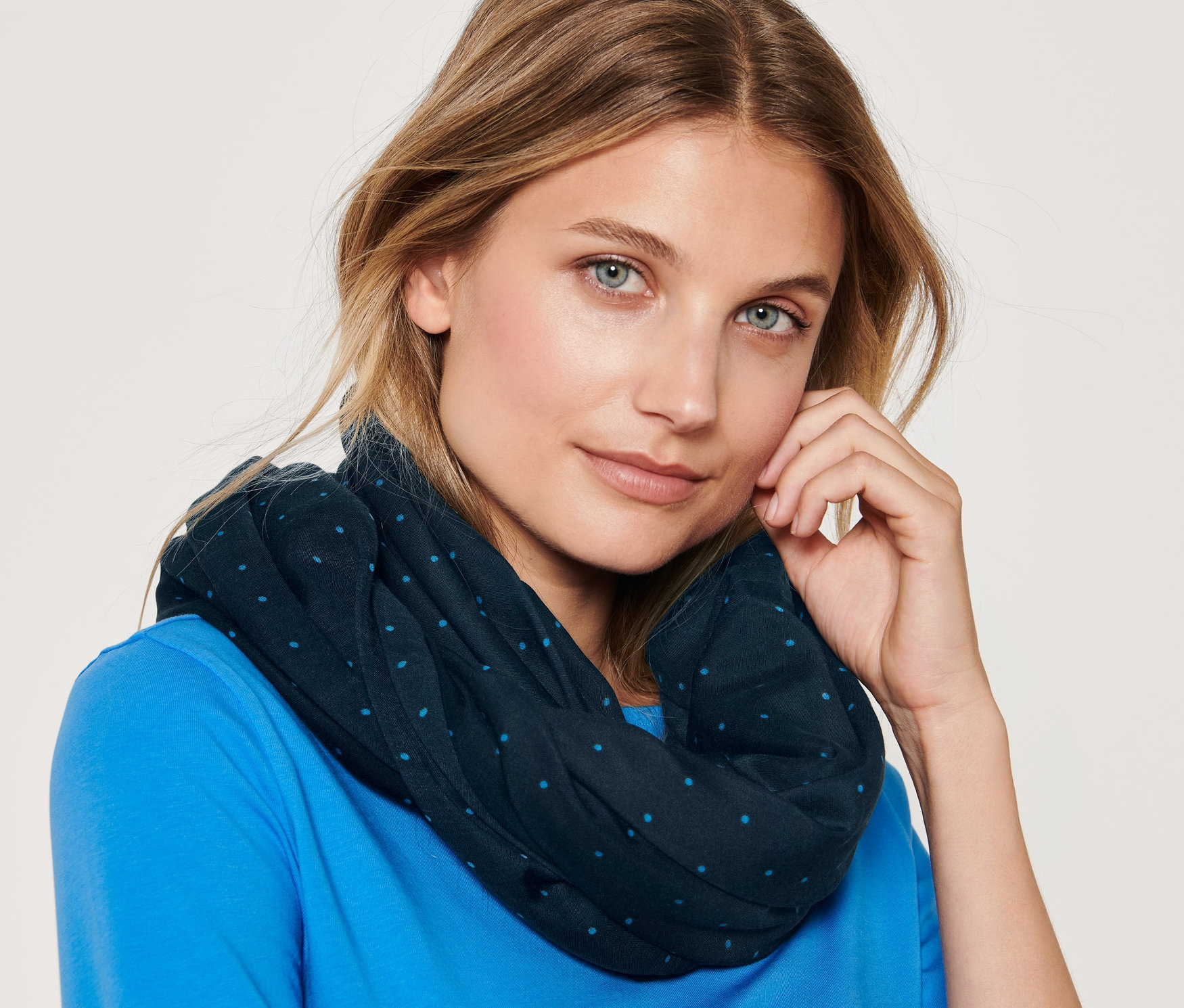 Portrait d'une femme blonde aux yeux bleus portant une écharpe-tube à pois et un t-shirt bleu.