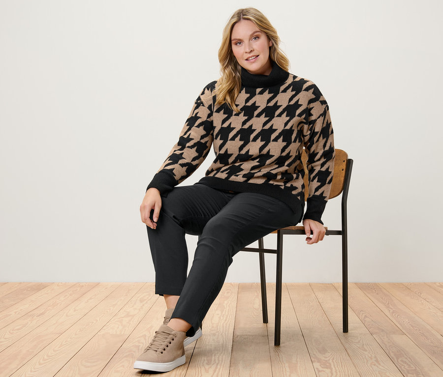 Femme assise sur une chaise portant un pull en maille à jacquard pied-de-poule et un pantalon stretch.