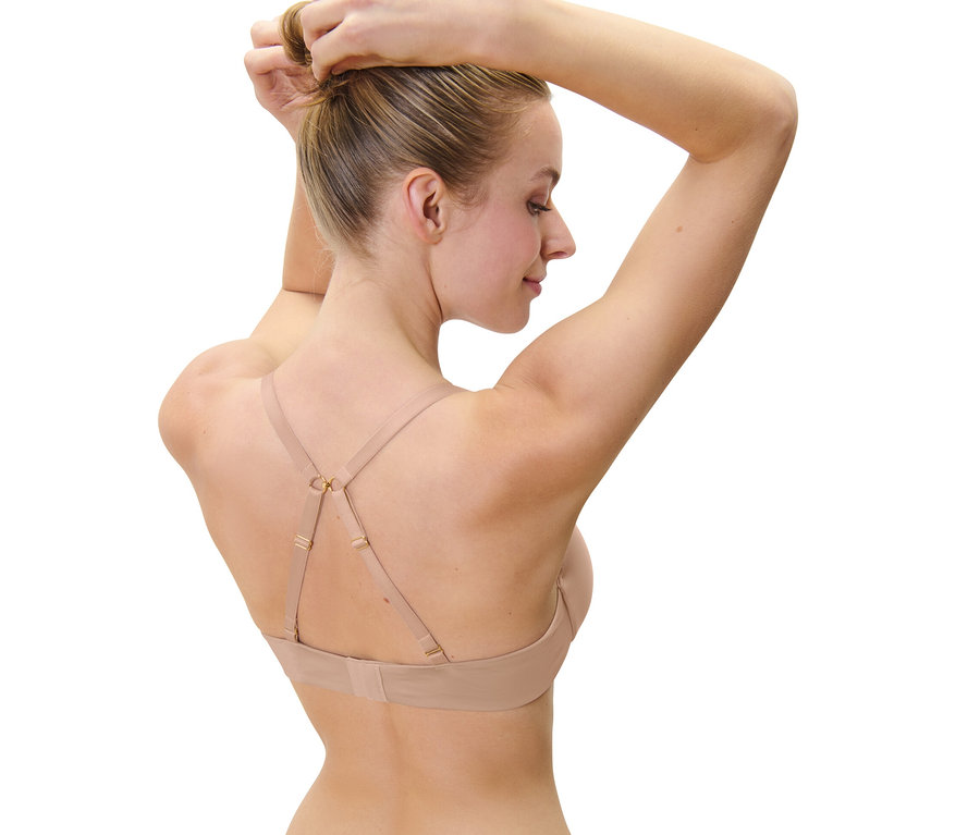Une femme attache ses cheveux en chignon et porte un soutien-gorge invisible beige.