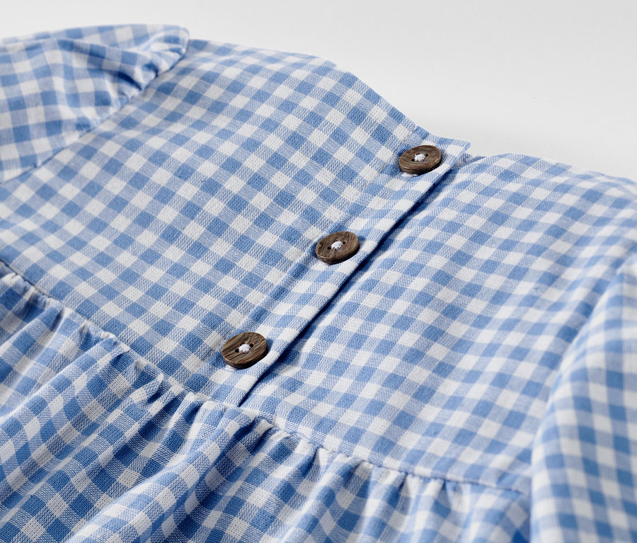 Gros plan d'une robe tissée pour enfant à carreaux bleus et blancs avec des boutons.