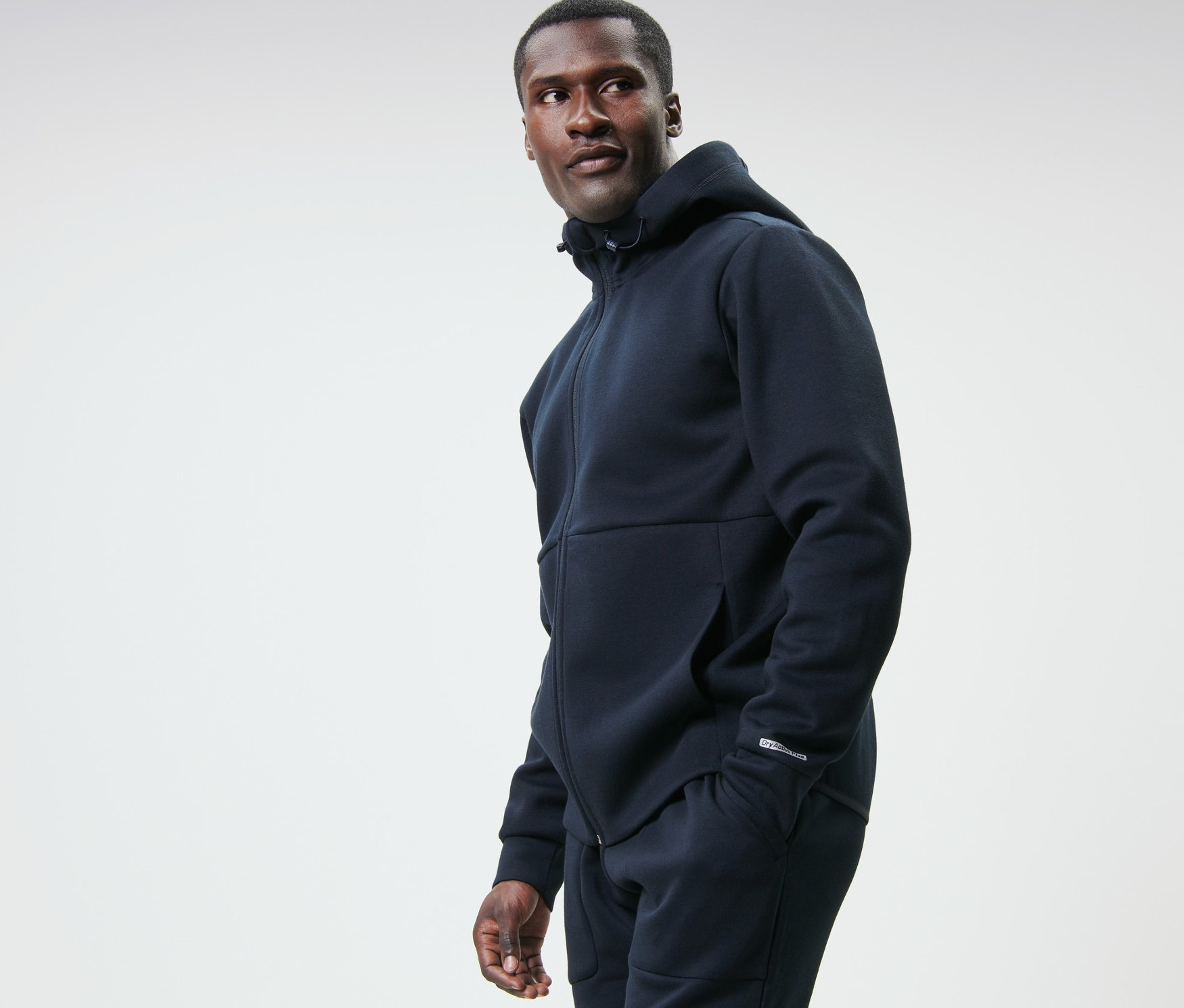 Un homme portant une veste de survêtement fonctionnelle bleu marine regarde vers la gauche.