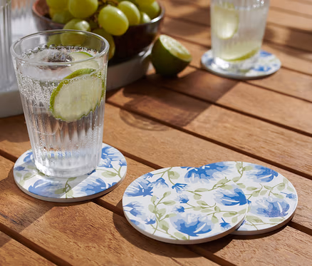Un verre avec une boisson est posé sur l'un des 4 sous-verres sur une table en bois.