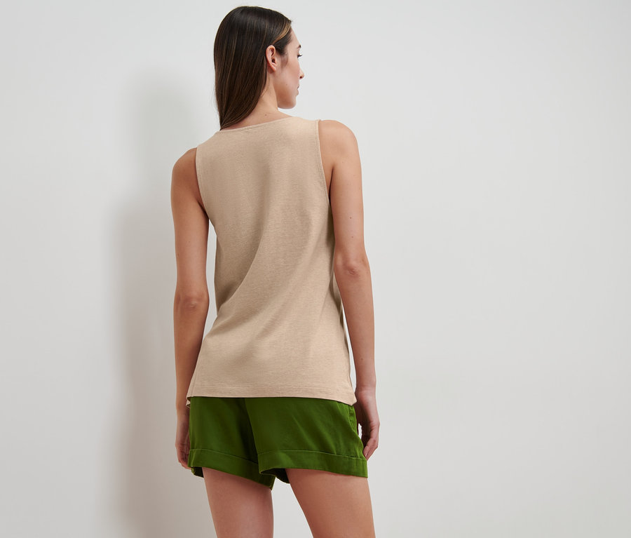 Une femme portant un haut beige chiné avec une patte de boutonnage et un short vert.