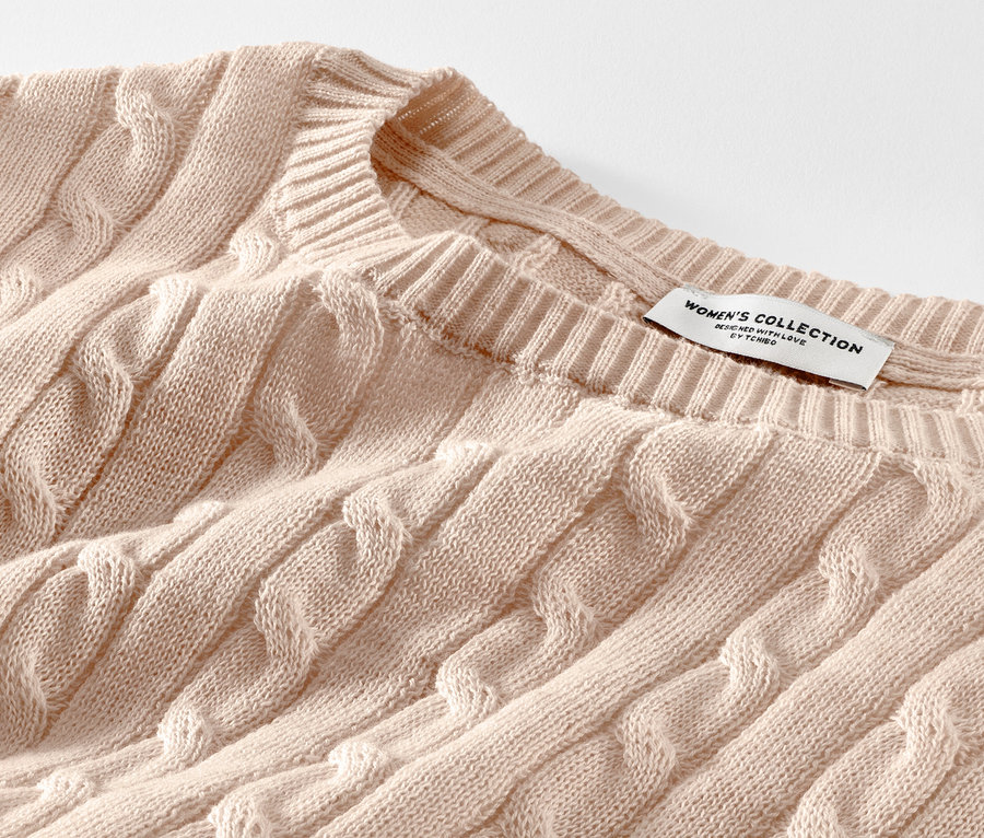 Gros plan sur un pull en maille torsadée crème.