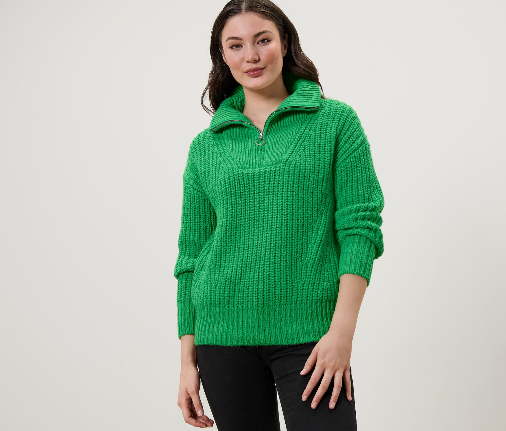 Une femme portant un pull camionneur en grosse maille vert avec un jean noir.